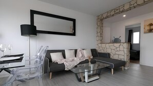 Una sala de estar moderna con una mesa de centro de vidrio, un sofá negro y una pared de acento de piedra.