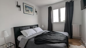 Un dormitorio moderno con cama, mesita de noche, lámpara y ventana con cortinas.