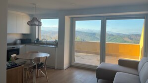 Ett modernt kök med matplats, stora fönster med utsikt över bergen och en balkong med en soffa.