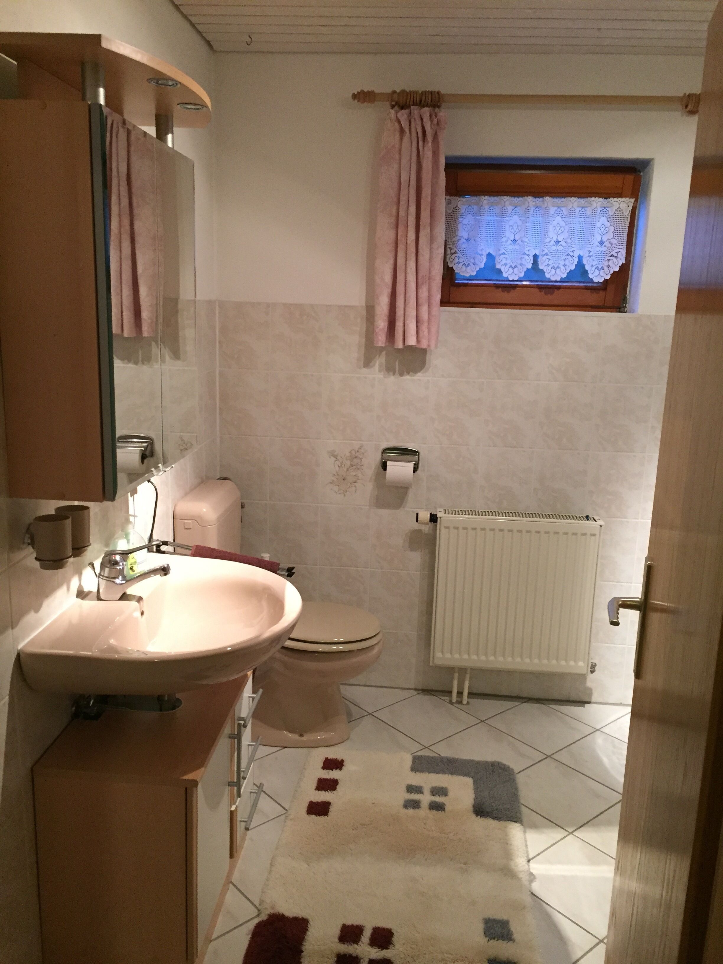 Un baño con lavamanos, inodoro y ventana con cortinas de encaje.