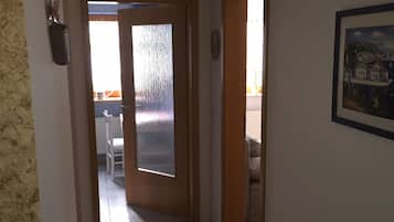 Un couloir doté d’un plancher en bois, une porte en verre donnant sur une pièce et un tableau encadré accroché au mur.