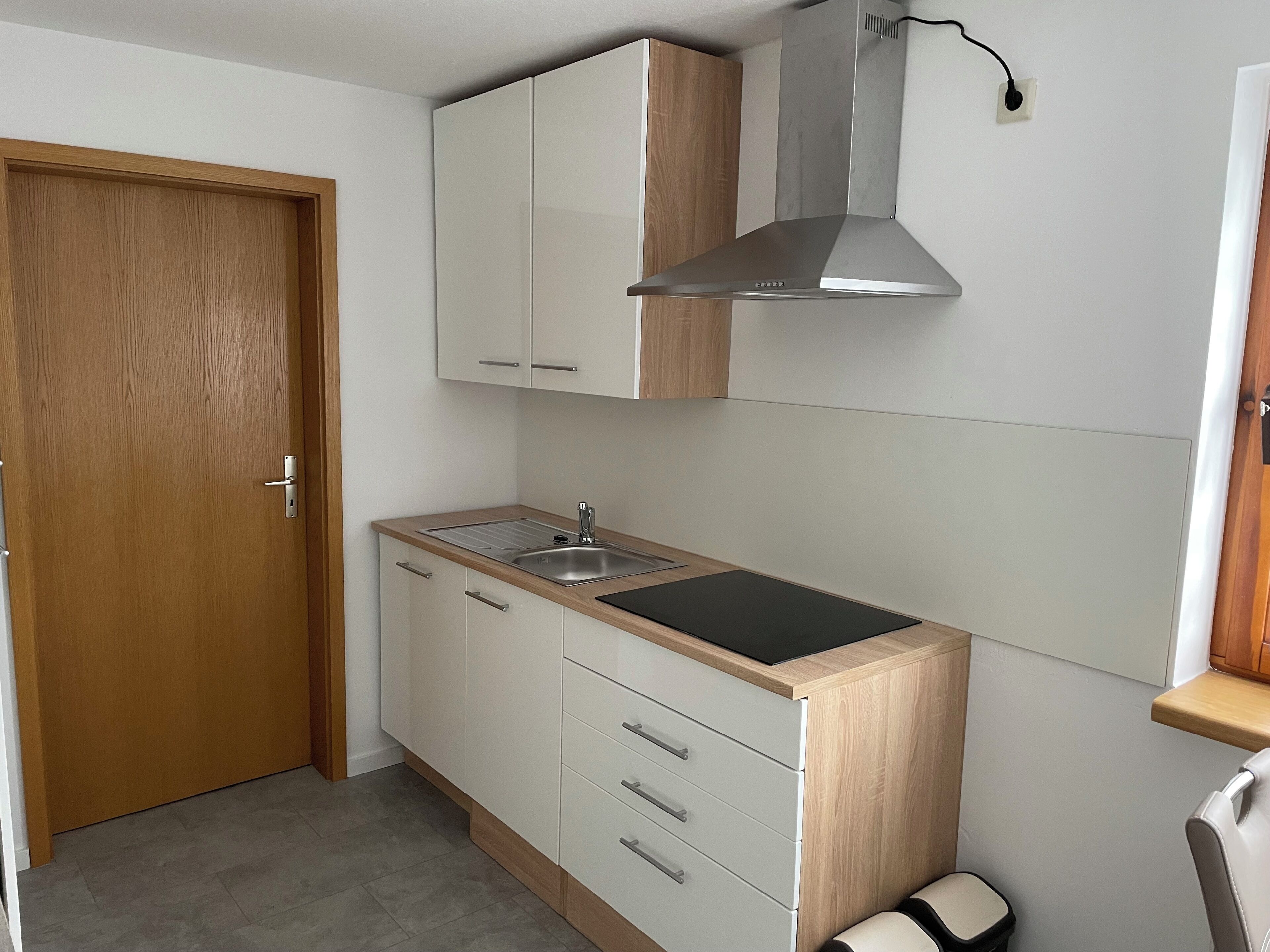 A compact kitchen with a wooden door, white cabinets, a stainless steel sink, and a black countertop.