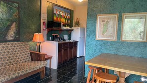 Ein Zimmer mit einer Couch, einem Esstisch mit Hocker, einer Küchenzeile und Bildern an den Wänden.