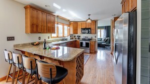 Una cocina moderna con armarios de madera, una isla grande con taburetes de bar, electrodomésticos de acero inoxidable y vistas al área de estar.
