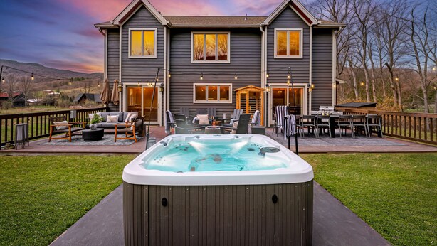 Casa de dos pisos con jacuzzi en el jardín delantero, mobiliario exterior y terraza.