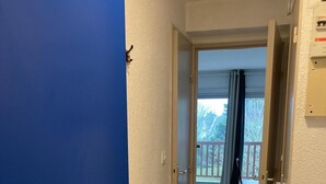 Un corridoio con una porta blu che dà su un balcone con vista su alberi e un parapetto.