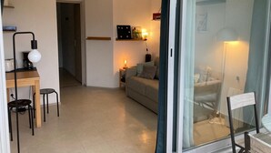 Un soggiorno moderno con un divano, un tavolino e una TV a parete. È presente una porta scorrevole in vetro che dà su un balcone.