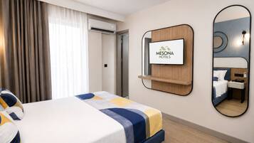Una habitación de hotel con una cama, un televisor montado en la pared, un espejo y un armario.