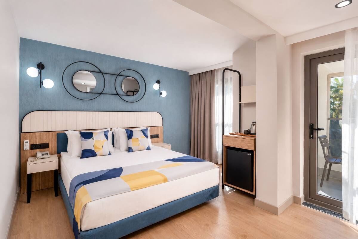 Une chambre d’hôtel moderne dotée d’un grand lit, de tables de chevet, d’un bureau et d’une porte-fenêtre coulissante donnant sur l’extérieur.