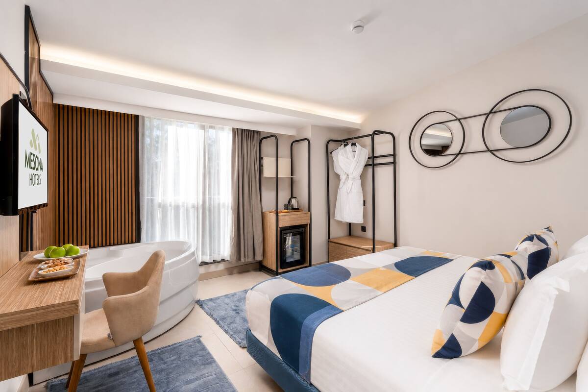Une chambre d’hôtel moderne équipée d’un lit, d’un bureau, d’une chaise, d’une baignoire et d’une petite table sur laquelle sont disposés des fruits.