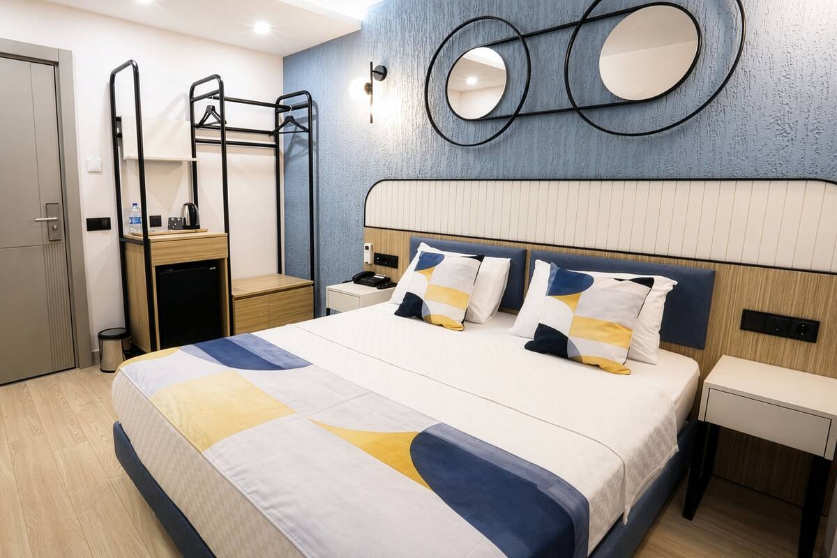 Une chambre d’hôtel avec un lit, des tables de chevet, un bureau, une armoire et un miroir au mur.