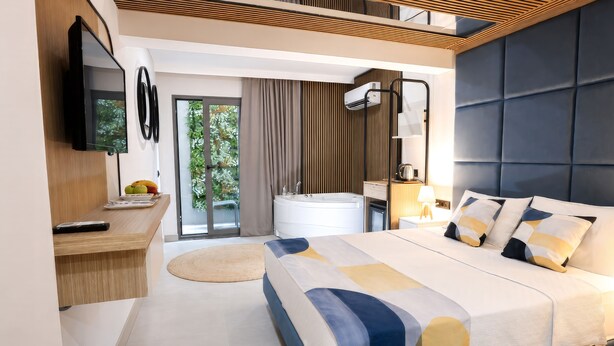 A modern hotel room with a bed, a desk, a TV, a bathroom, and a view of greenery. - Mesona Hotels Blue Hill (Konyaalti)