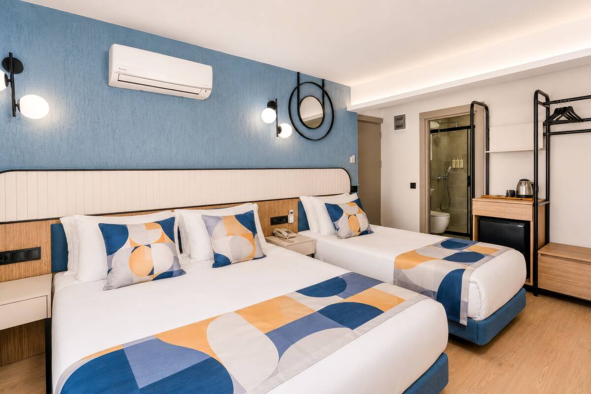 Une chambre d’hôtel avec deux lits, un petit bureau, un miroir et un espace douche.