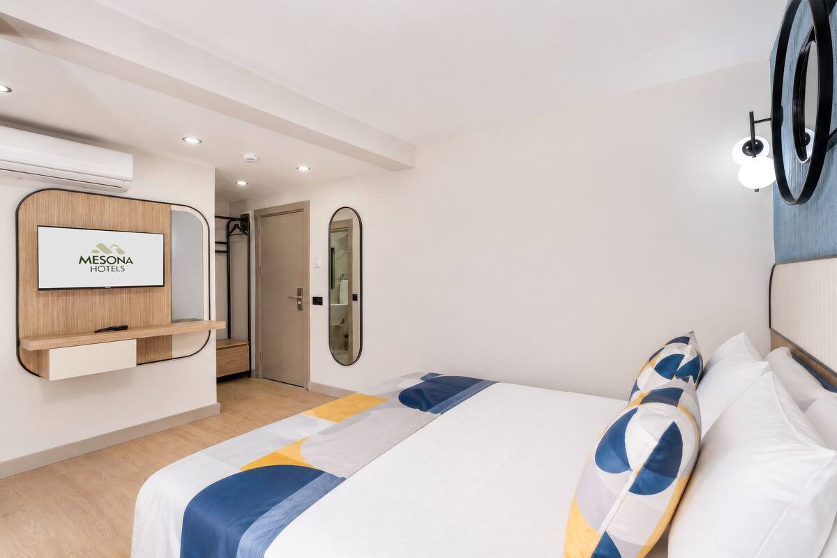 Une chambre d’hôtel avec un lit, un téléviseur fixé au mur, un miroir et une porte donnant sur une salle de bain.