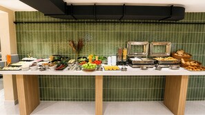 Une table de buffet garnie de divers plats, avec un mur recouvert de carreaux verts en arrière-plan.