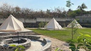 A campsite with several tents set up on a grassy area, surrounded by a stone wall and trees. - Glamphouse, adventure and relaxation! (Oaxtepec)