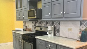 Una cocina con gabinetes grises, una estufa negra, una cafetera y un tapete estampado.