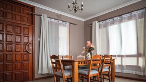 Un comedor con una mesa y sillas de madera, un florero con flores y un gran puerta de madera.