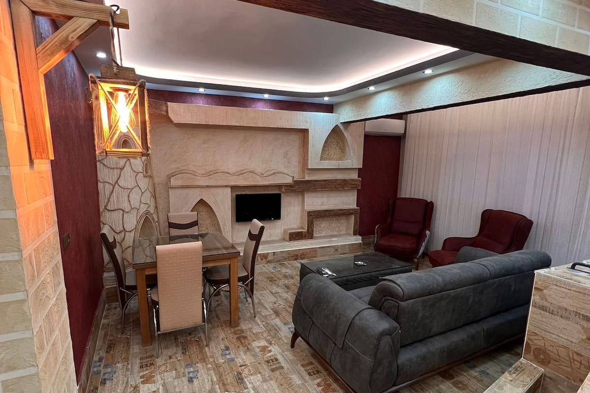 A cozy living room with a fireplace, a sofa, a dining table with chairs, and a TV mounted on the wall.