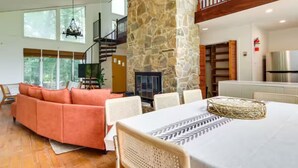 Amplia sala de estar con chimenea de piedra, un sofá grande y una mesa de comedor.