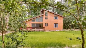 Una casa moderna de madera con ventanas amplias, rodeada de un jardín cubierto de césped y árboles.