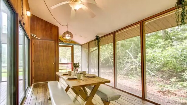 Una mesa de comedor de madera con bancos, ventanas amplias y un ventilador de techo.