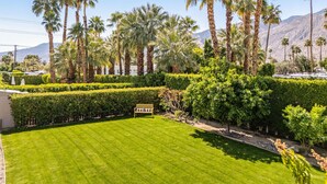 A well-maintained garden with a lawn, palm trees, and neatly trimmed hedges. - Oasis Del Sol | by Rather Be Properties (Palm Springs)