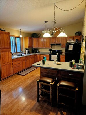 A kitchen with wooden cabinets, a black refrigerator, a countertop with various items, and a hanging light fixture.