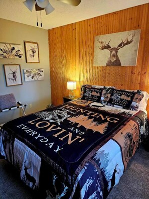 A bedroom with a large bed, wooden panel walls, and multiple framed deer artwork.