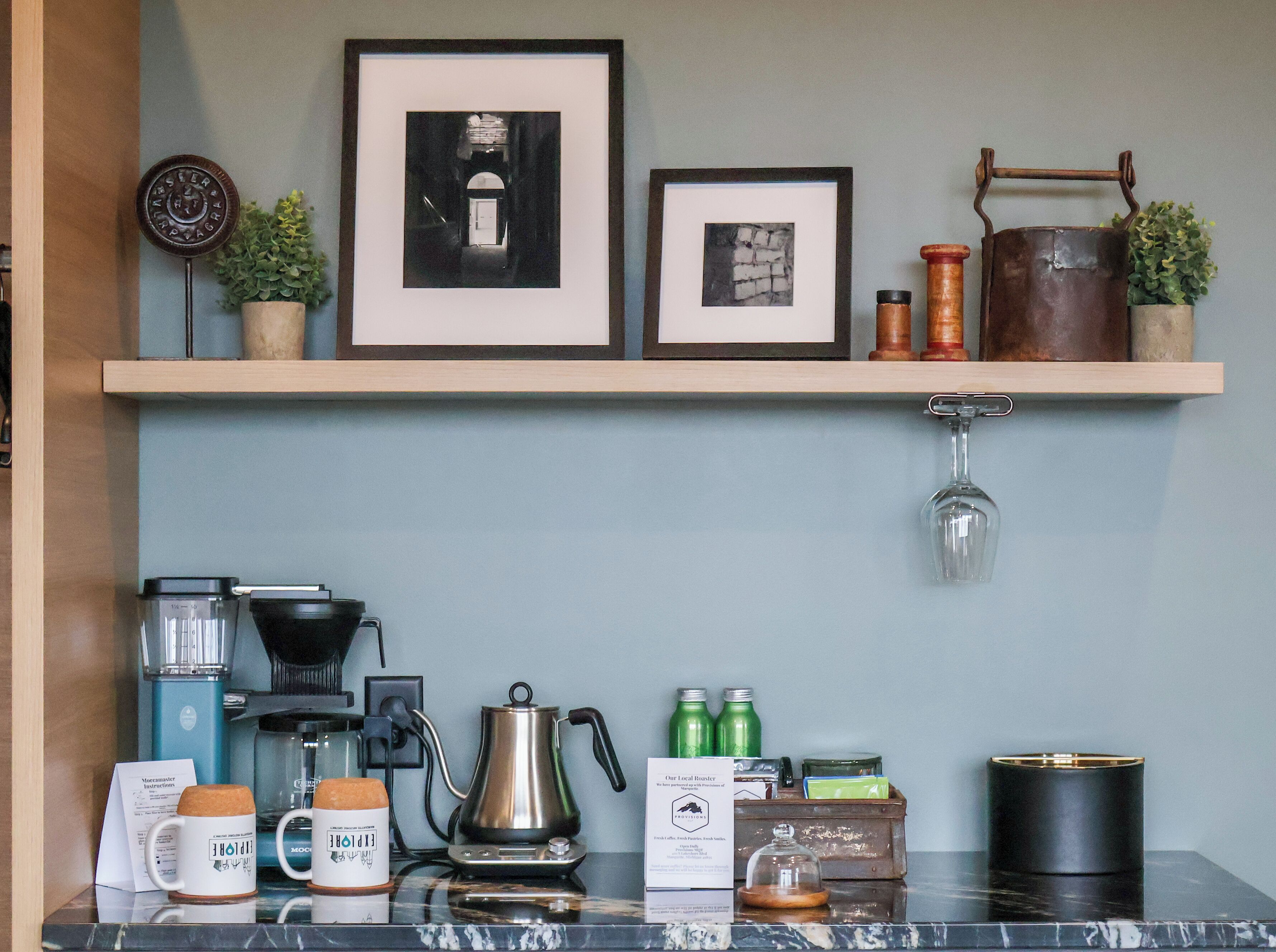 A coffee station with a coffee maker, kettles, mugs, and a menu sign.