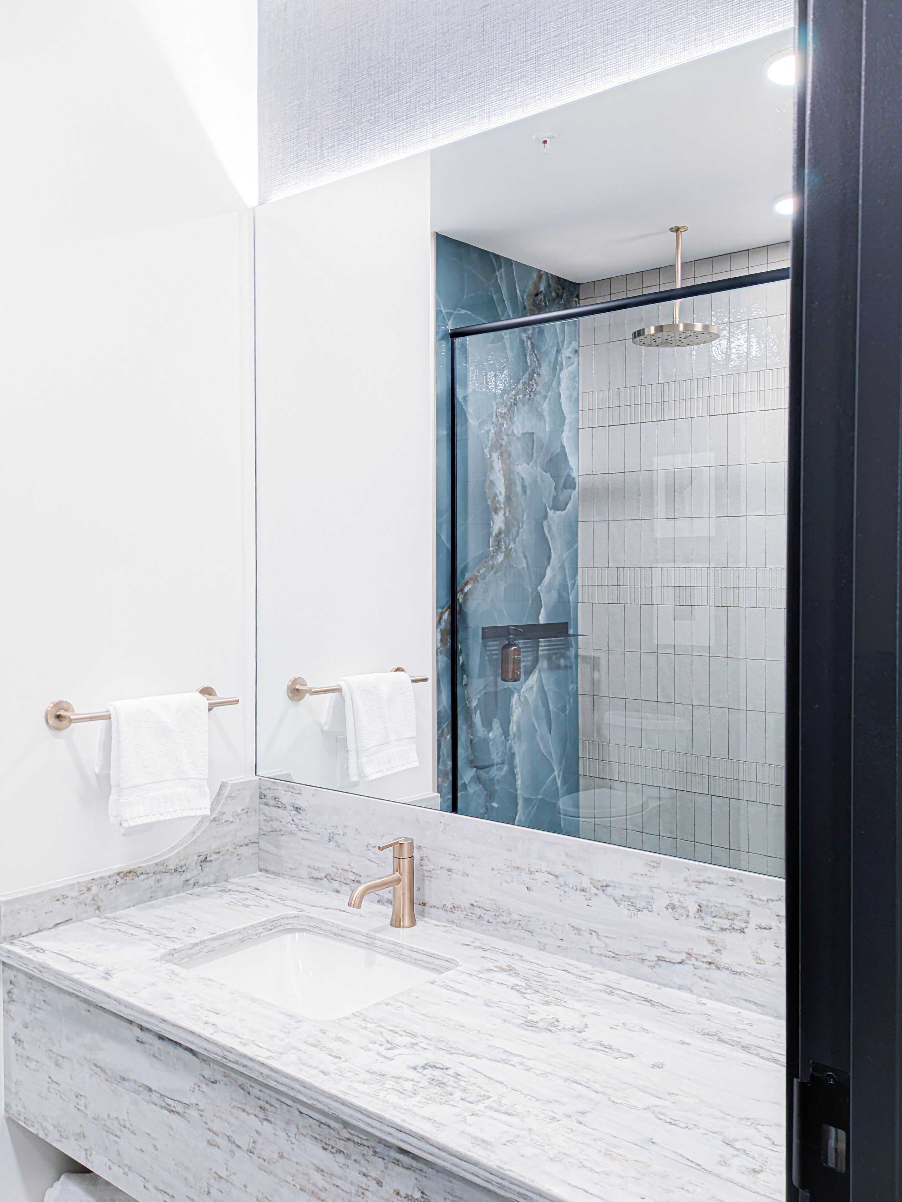 Un baño moderno con un lavabo de mármol, cabina de ducha con paredes de vidrio y un espejo grande.
