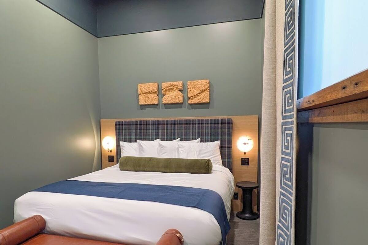 Un dormitorio con cama, lámparas de noche, un banco y decoración mural.