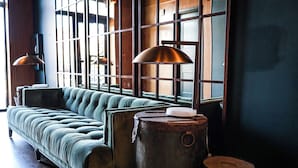 A green upholstered sofa, a metal drum, and a wooden table in a room with large windows and a dark wall. - EXPLORE Marquette Historic District (Marquette)