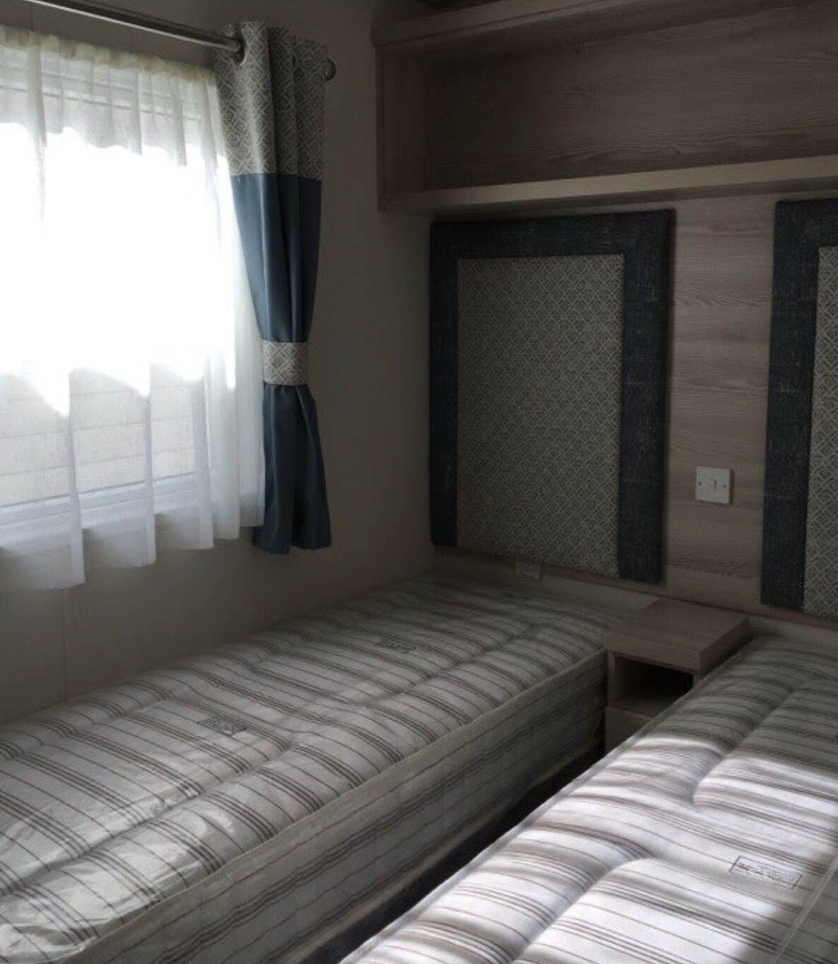 Ein kleines Zimmer mit einem Einzelbett, einem Fenster, einem Vorhang und einem gemusterten Kopfteil.
