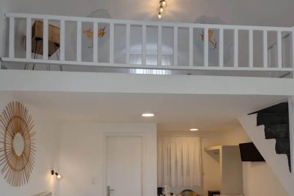 A hotel room with a large bed, a smaller bed, a sofa, a desk, and a staircase.