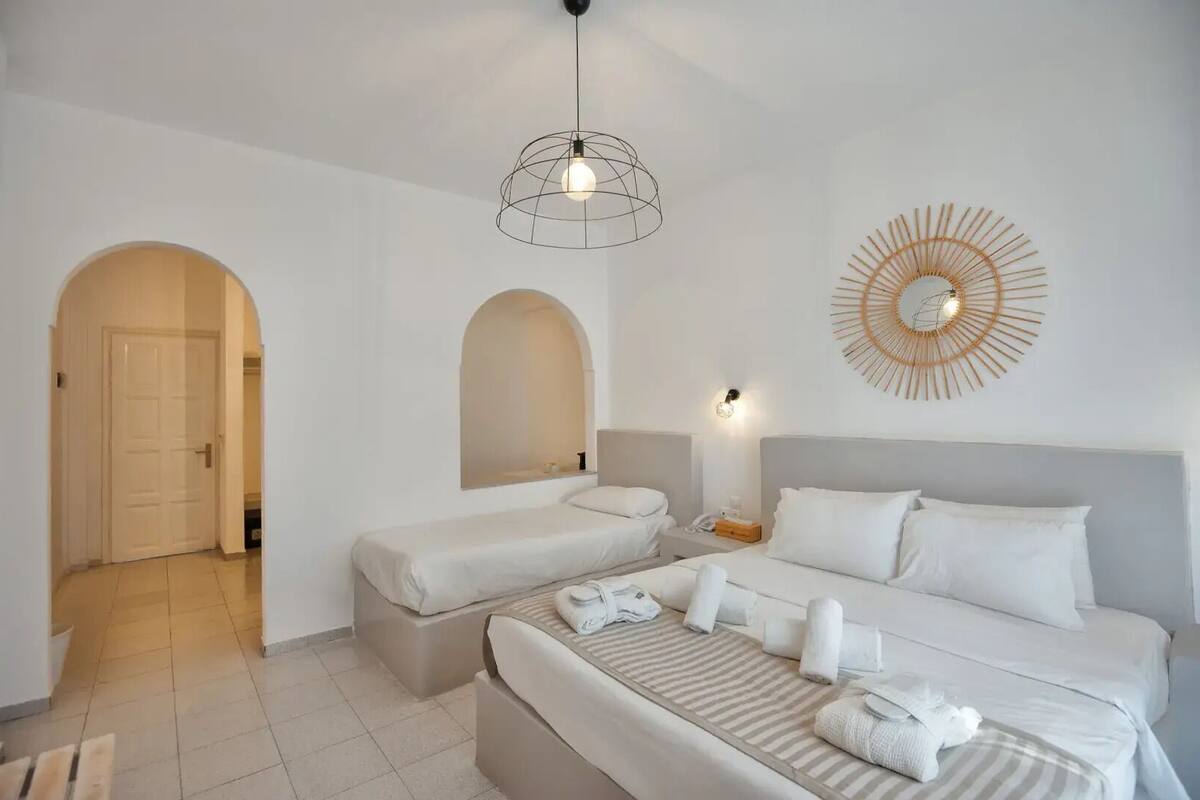 A hotel room with two beds, a large mirror, a wall-mounted light fixture, and a decorative sunburst wall art piece.