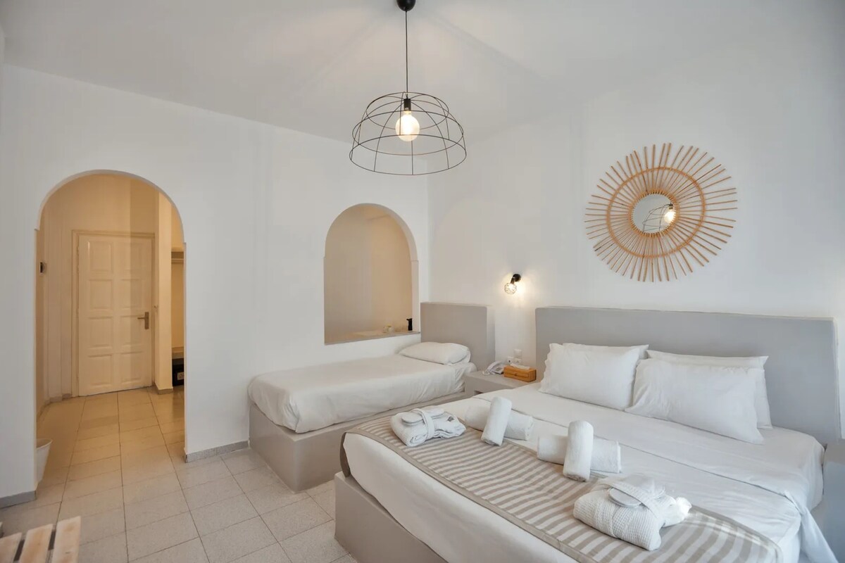 A hotel room with two beds, a large mirror, a wall-mounted light fixture, and a door leading to another room.