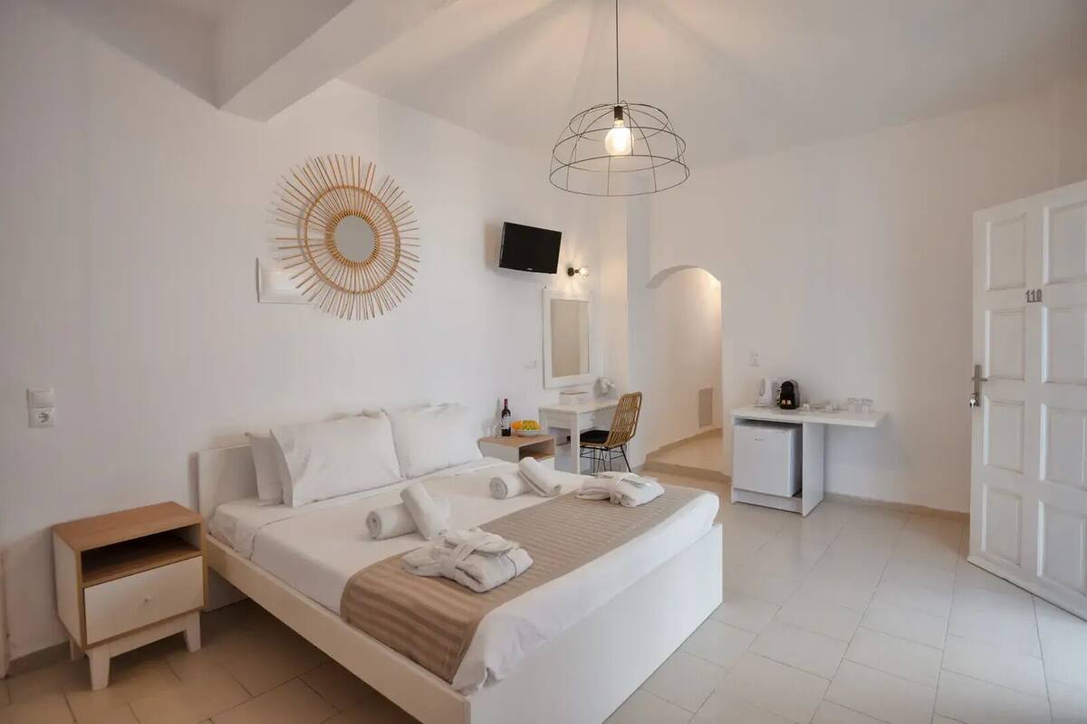 A modern hotel room with a large bed, a desk, a chair, a TV, and a door with the number 110.