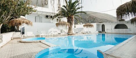 A swimming pool with a stone border, white lounge chairs, and a palm tree.