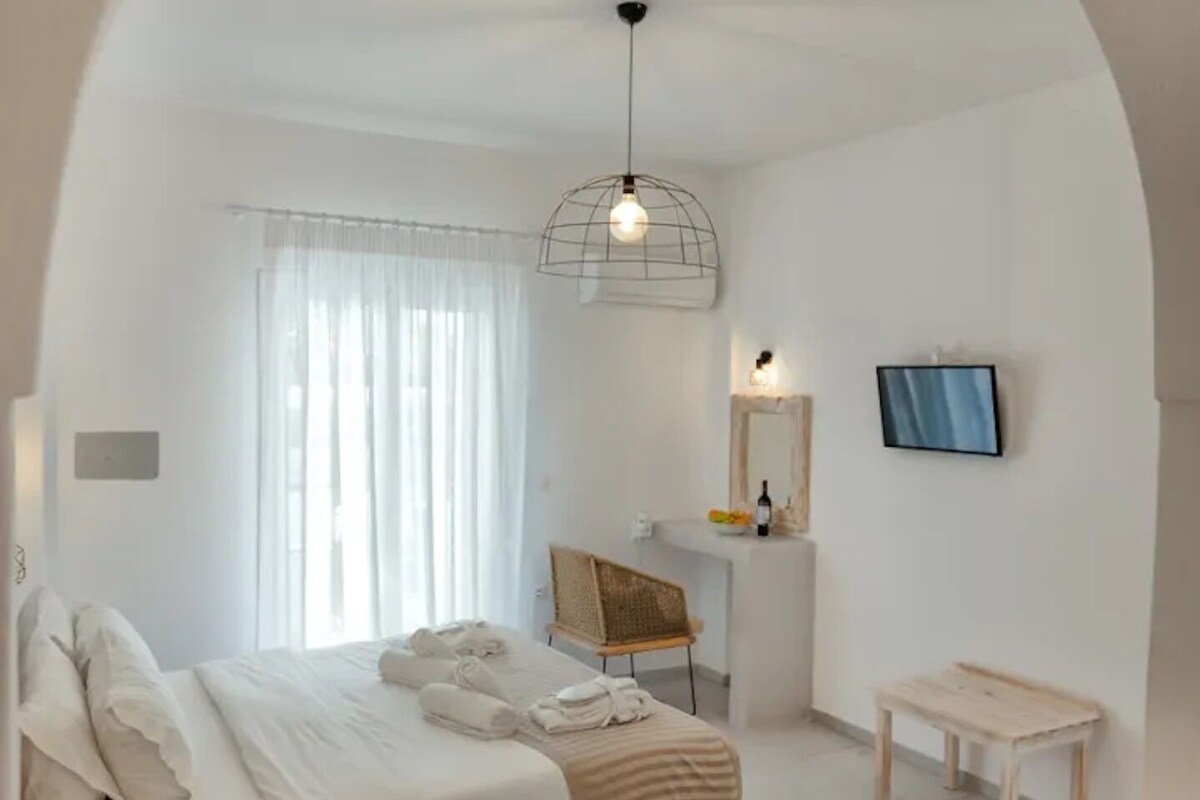 A minimalist hotel room with a bed, desk, and TV.