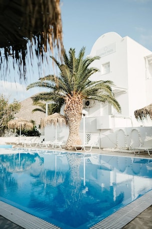 Una piscina con sillas de descanso, una palmera y un edificio blanco con un letrero.