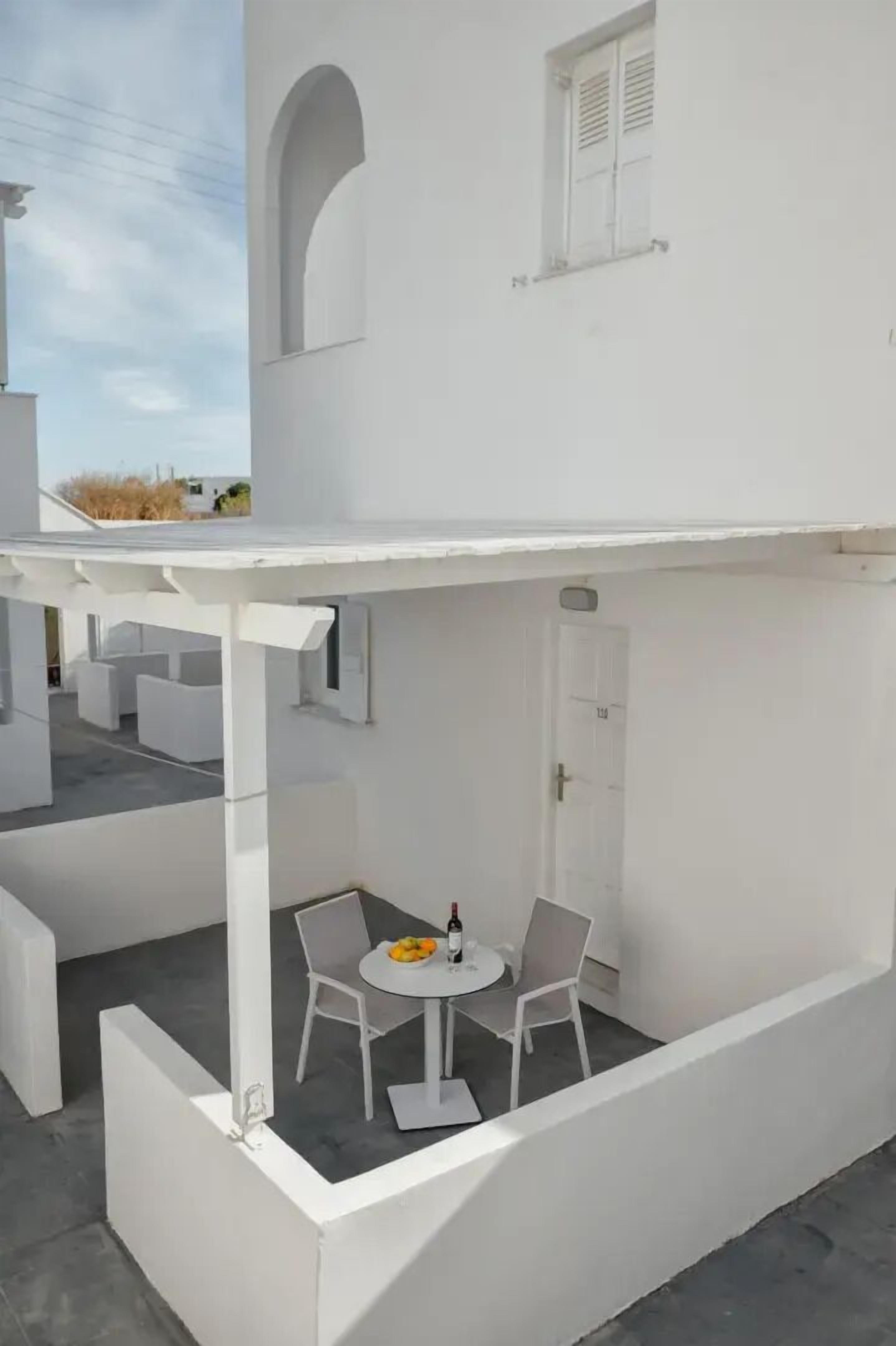 A white building with a covered outdoor seating area, a door, and a window.