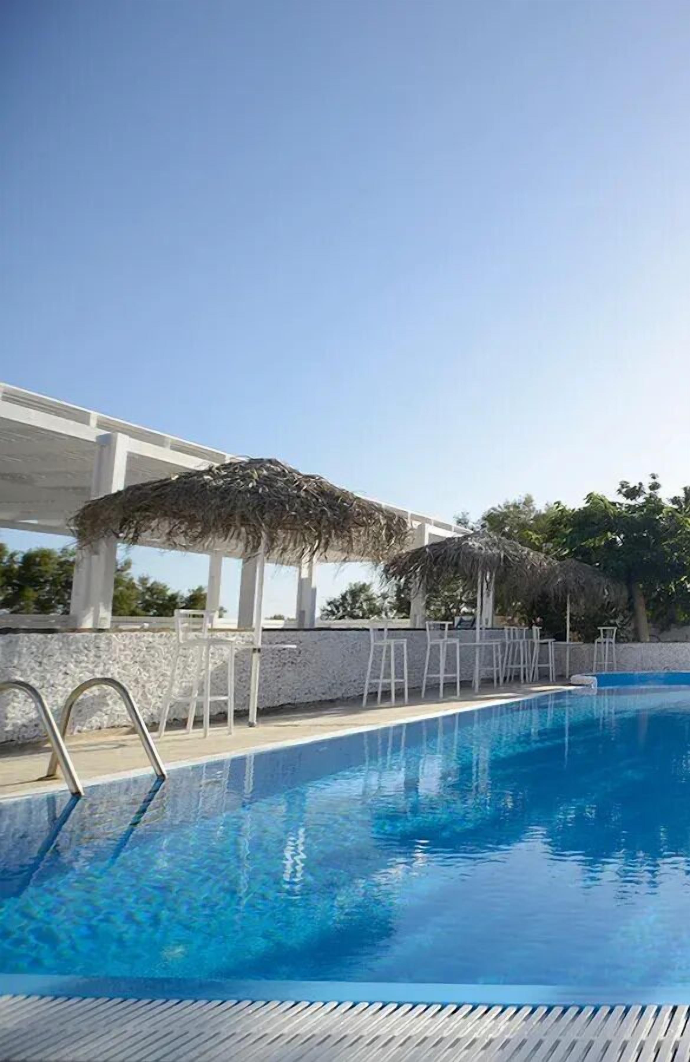 A swimming pool with a clear blue water surface, surrounded by white lounge chairs and a thatched umbrella structure.