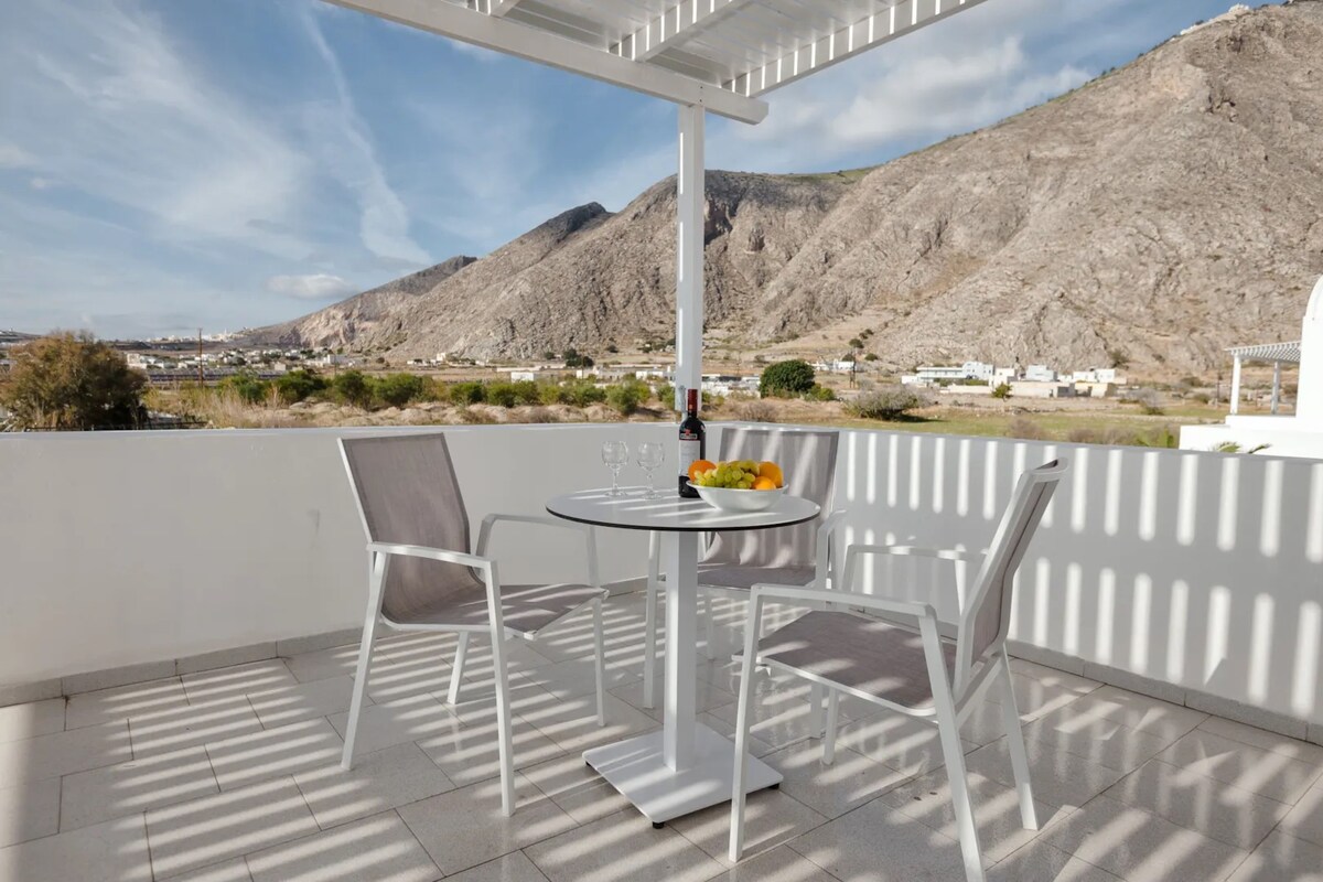 A terrace with a table, chairs, and a view of a mountainous landscape.
