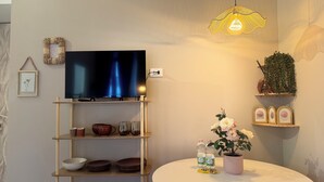 A living room with a flat-screen TV on a wooden stand, a round table with a potted plant, and a hanging light fixture. - LaReginadelleLocazioni in Porta Romana 2 (Milan)