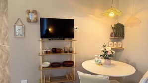 A living room with a flat-screen TV, wooden shelves with bowls and glasses, a round table with a potted plant, and a hanging light fixture. - LaReginadelleLocazioni in Porta Romana 2 (Milan)