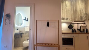 A modern bathroom with a mirror, sink, and toilet. There is a wooden rack and a small shelf. The kitchen has a stove, oven, and various utensils. - LaReginadelleLocazioni in Porta Romana 2 (Milan)