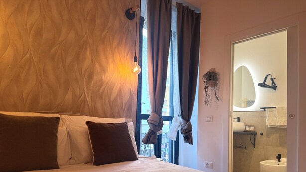 A hotel room with a bed, a window with curtains, a bathroom with a sink and mirror, and a wall-mounted hairdryer. - LaReginadelleLocazioni in Porta Romana 2 (Milan)