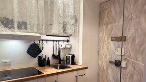 A modern kitchen with a wooden countertop, stainless steel sink, and white cabinets. There is a window with sheer curtains, a hanging rack with utensils, and a built-in oven. - LaReginadelleLocazioni in Porta Romana 2 (Milan)