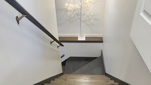 Una escalera de madera con barandilla de metal, que lleva a un rellano con pared blanca y un árbol decorado con luces.